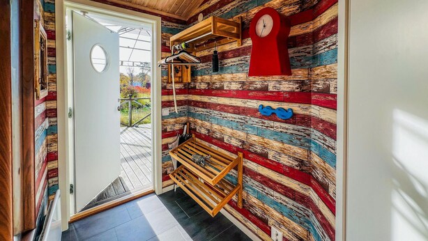Une pièce avec un banc en lattes de bois, une horloge rouge au mur et un mur en bois aux couleurs vives.