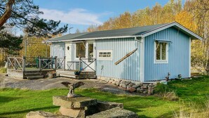 Une petite cabane à un seul étage, dotée d’un porche, de fondations en pierre et d’une terrasse en bois.