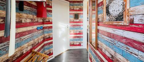 A narrow hallway with a wooden floor and walls painted in a striped pattern of red, blue, and white.