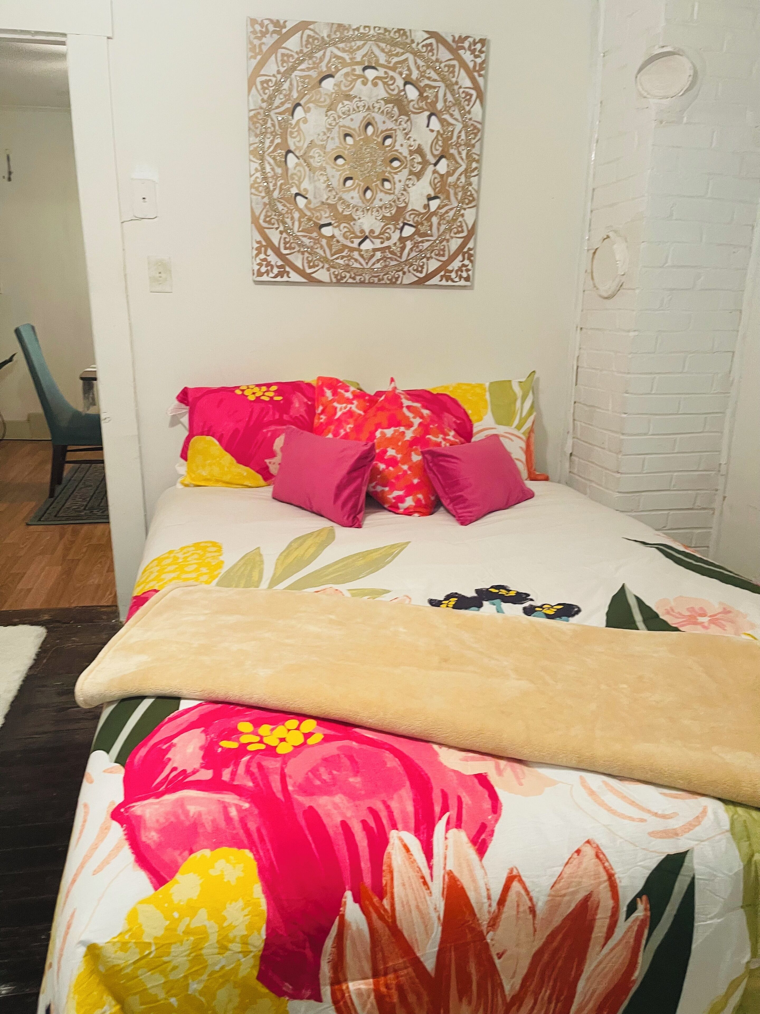 A bed with a floral bedspread, multiple pillows, and a decorative wall hanging.