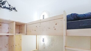 Ett rum med en våningssäng, där den övre sängen är gjord av trä och den nedre är en vanlig säng. På väggen finns en stor väggdekor som föreställer ett berg.