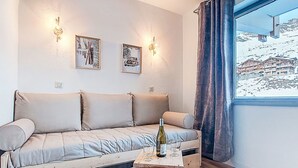 Ett mysigt rum med en soffa, ett litet träbord med en flaska och glas, och två väggmonterade lampor.