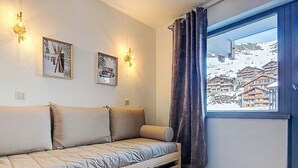 Ett mysigt rum med en soffa, två väggmonterade lampor och ett fönster med utsikt över ett snötäckt berg.