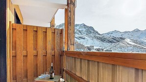 Ein Holzbalkon mit Tisch und Flasche, mit Blick auf eine verschneite Berglandschaft.
