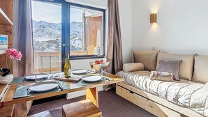 Ein gemütliches Zimmer mit einem hölzernen Bett, einem Esstisch für zwei Personen und einem großen Fenster mit Blick auf die Berge.