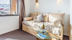 Ein Schlafzimmer mit einem Bett, einem Fenster mit Vorhängen, einem Nachttisch mit Flasche und Gläsern sowie Wandleuchten.