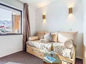 A bedroom with a bed, a window with curtains, a bedside table with a bottle and glasses, and wall-mounted lights. - Les Olympiades by Interhome (Val Thorens)