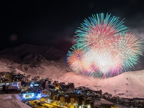 A snow-covered mountain town with illuminated buildings and a large fireworks display in the sky. - Les Olympiades by Interhome (Val Thorens)