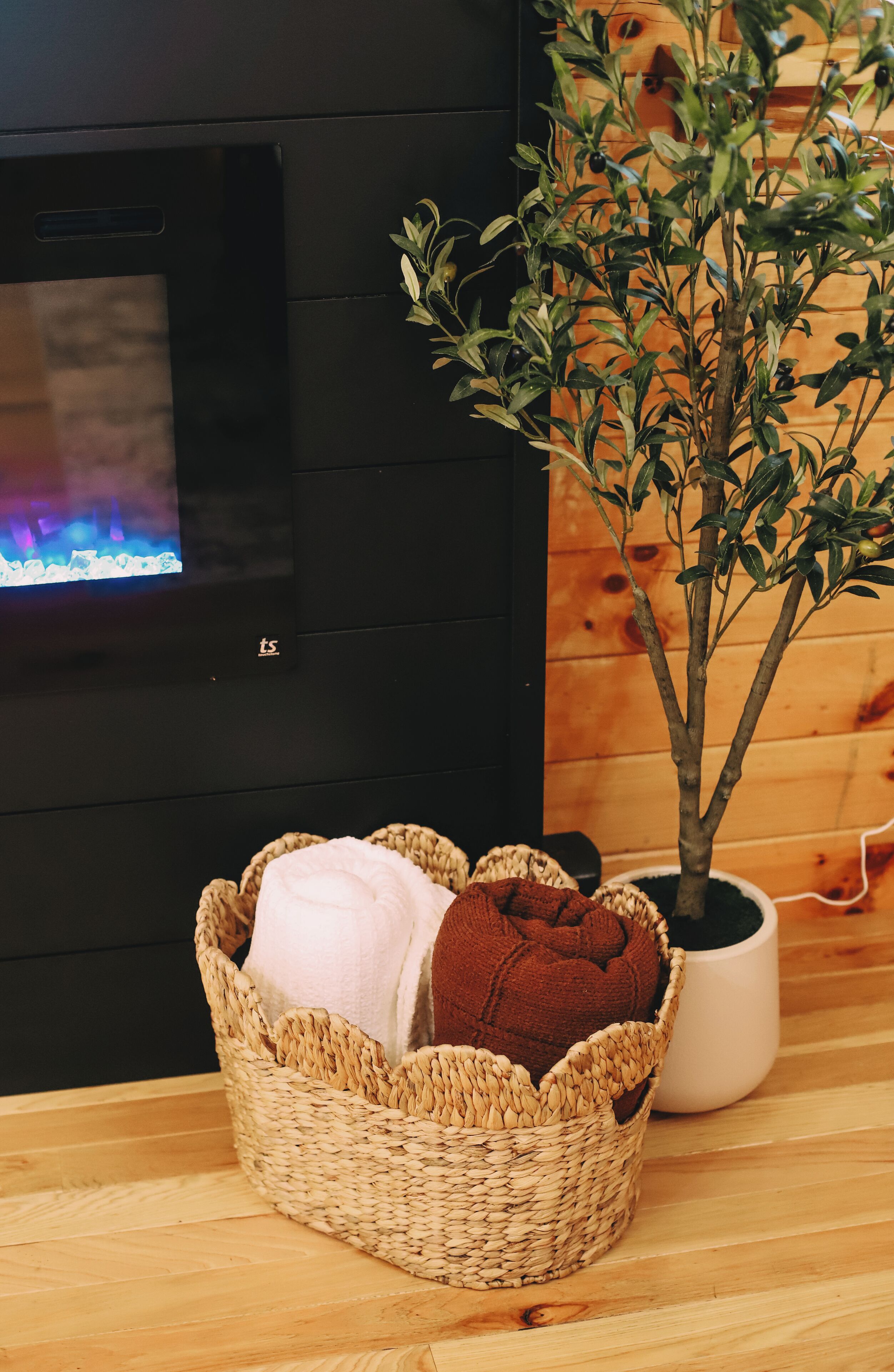 A room with a fireplace, a woven basket with towels, and a potted plant.