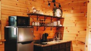 A compact kitchen with wooden walls, a refrigerator, a microwave, and a sink.