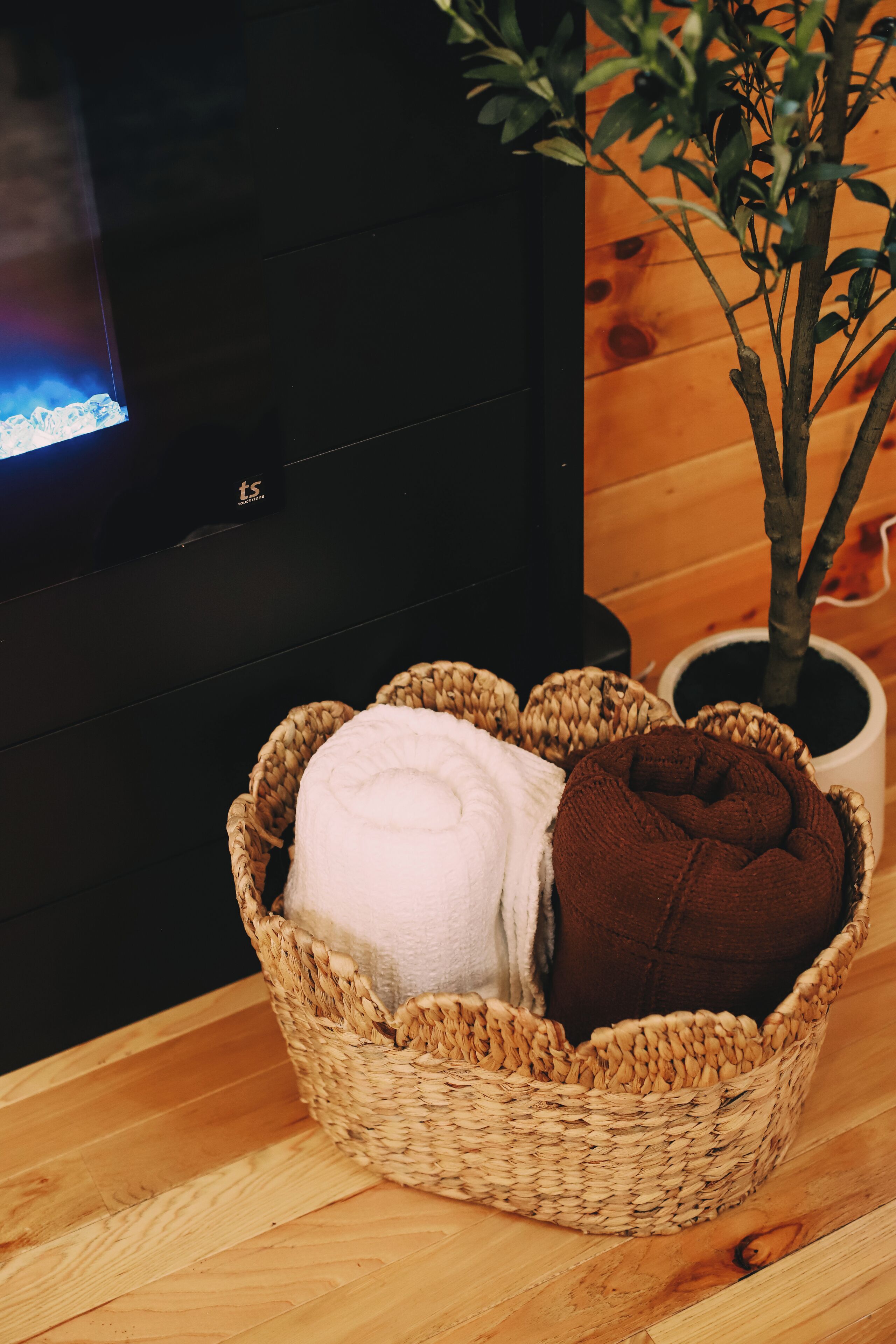 A woven basket with two towels, a potted plant, and a television on a wooden floor.