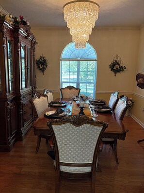 A dining room with a large wooden table, ornate chairs, a chandelier, and a view through a large window. - Spacious Oxford Retreat Only 7 minutes from Ole Miss on 1.2 acres (Oxford)