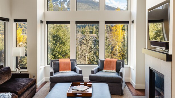 Un soggiorno spazioso con soffitto alto, ampie finestre che offrono vista sulle montagne, un caminetto e un moderno impianto TV.
