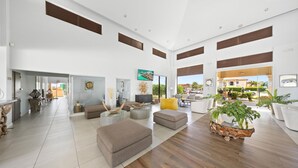 A spacious living area with a large window, a sofa, a coffee table, and a plant. - 2BR3BA Retreat in Gated Community w/ Pools ~ GYM (Noord)