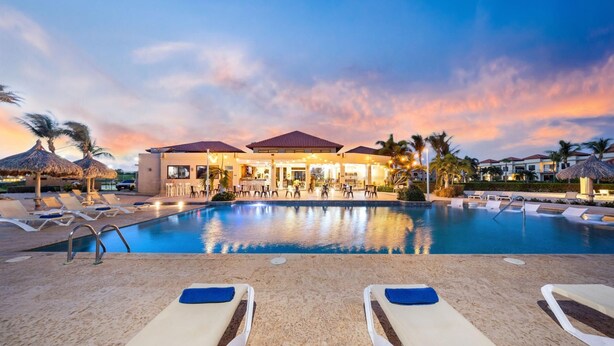 A resort pool area with lounge chairs, a bar, and a building with a red roof. - 2BR3BA Retreat in Gated Community w/ Pools ~ GYM (Noord)