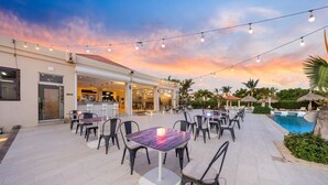 An outdoor dining area with tables and chairs, a pool, and a building with a bar. - 2BR3BA Retreat in Gated Community w/ Pools ~ GYM (Noord)