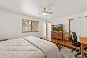 A bedroom with a bed, a desk, a chair, a dresser, and a ceiling fan. - Leaf & Needle | Single-Story Cabin, Fenced Yard, Wood Stove & Near The Village (Big Bear Lake)