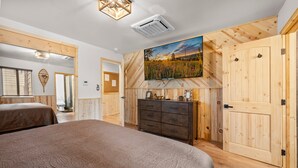 Ein Schlafzimmer mit einem großen Bett, Holzwänden, einem Schminktisch und einem Gemälde von einem Feld.
