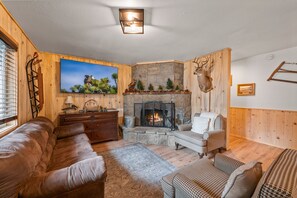 Un salon chaleureux avec une cheminée en pierre, des murs en bois et une tête de cerf accrochée au mur.
