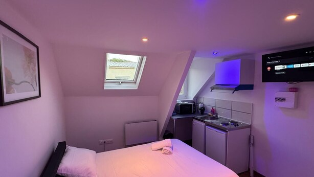 A compact bedroom with a bed, a small kitchenette, a TV, and a window. - Comfort Appart 3 (Calais)