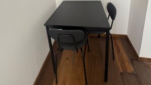A room with a black table and two chairs, a flat-screen TV mounted on the wall, and wooden flooring. - Comfort Appart 3 (Calais)