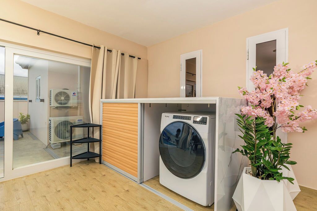 A compact laundry room with a washing machine, a drying rack, and a potted plant.