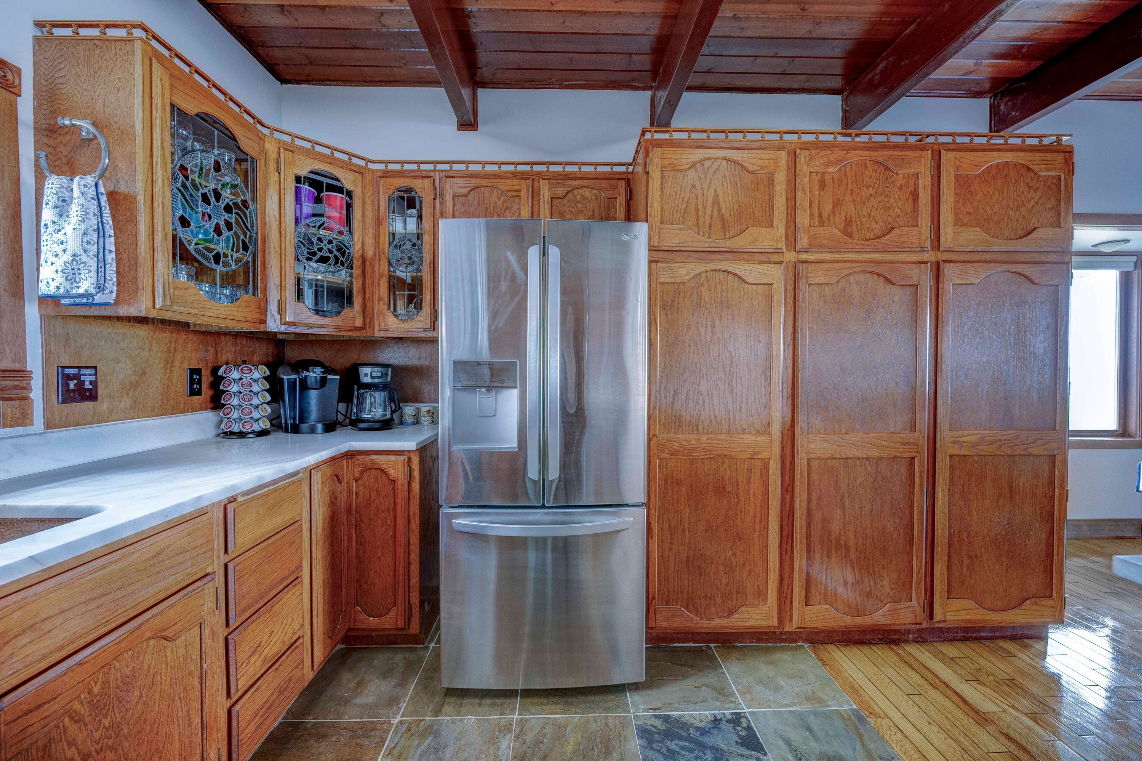 A kitchen with wooden cabinets, a stainless steel refrigerator, and a tiled floor.