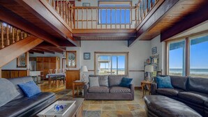 A spacious living area with a high ceiling, a balcony, and a view of the beach. - Serenity at South Beach (Westport)
