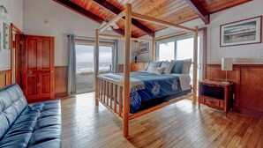 A bedroom with a wooden four-poster bed, a sofa, and a view of the sea. - Serenity at South Beach (Westport)