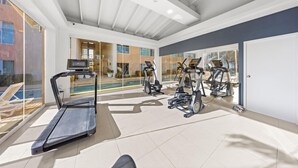 Een moderne fitnessruimte met loopbanden, elliptische trainers en een zwembadgedeelte, zichtbaar door grote ramen.
