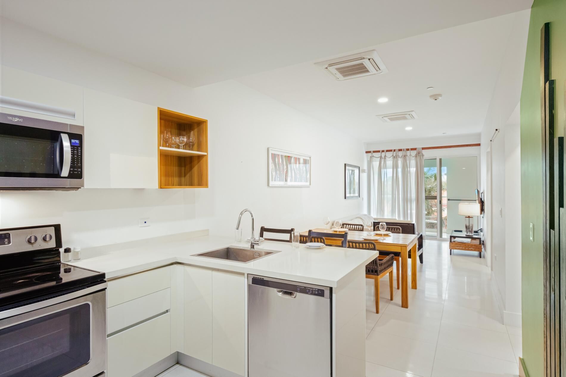 Una cocina moderna con microondas, horno y lavavajillas integrados. Cuenta con una zona de comedor con mesa y sillas, y vistas al exterior a través de una puerta corrediza de vidrio.