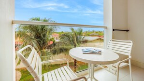 Een balkon met witte stoelen en een tafel, met uitzicht op een woongebied met huizen en palmbomen.