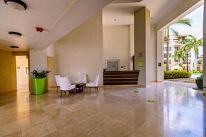 A hotel lobby with a reception desk, seating area, and a large green planter. - Modern 2BR 2BA Condo on Top Floor w/ Amazing Views (Noord)