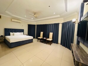 Ein Hotelzimmer mit einem großen Bett, einem Schreibtisch mit Stuhl, einem Fernseher und dunklen Vorhängen.
