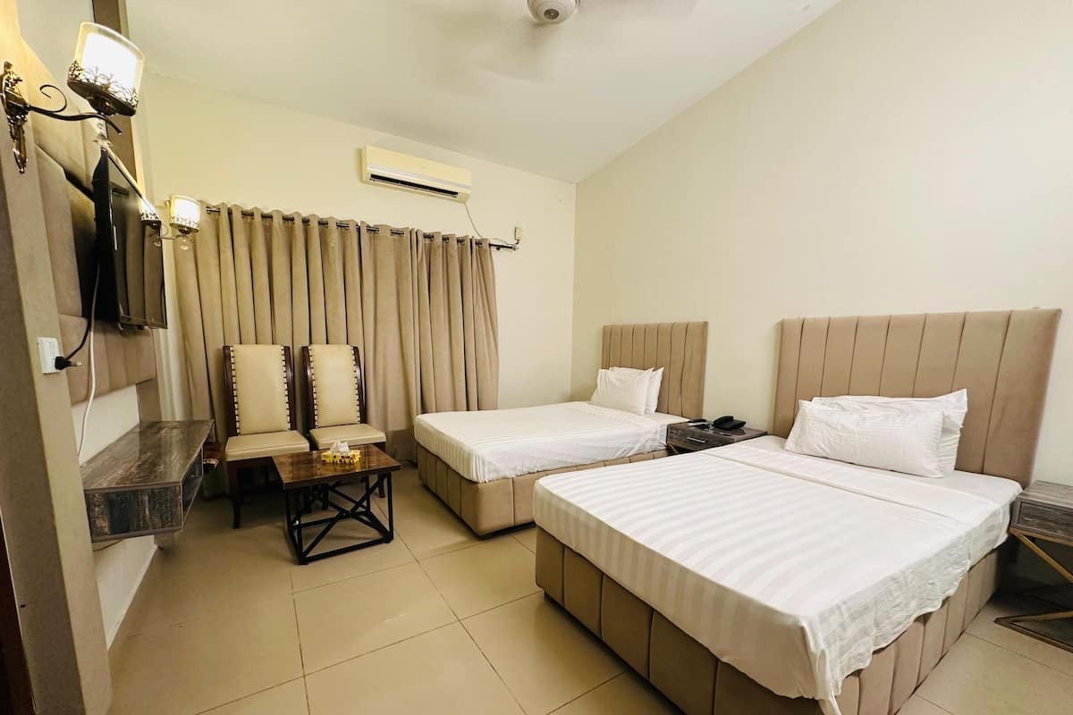 A hotel room with two beds, a desk, chairs, and a TV.