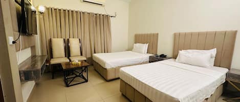 A hotel room with two beds, a desk, chairs, and a TV.