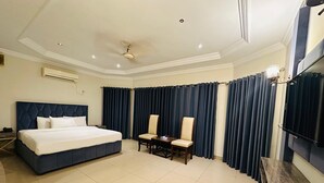 Een hotelkamer met een groot bed, een bureau met stoel, een televisie en donkere gordijnen.