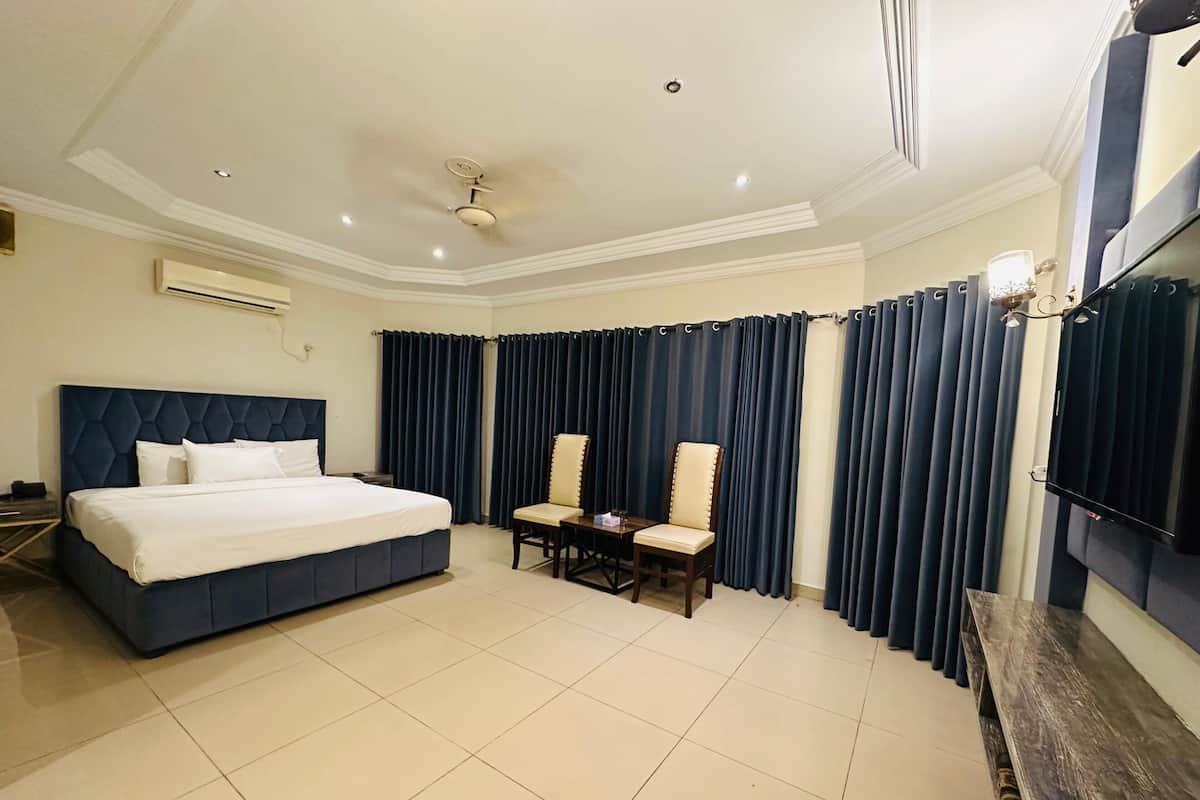 A hotel room with a large bed, a desk with a chair, a TV, and dark curtains.