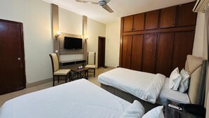 Een hotelkamer met twee eenpersoonsbedden, een bureau met stoel, een wandtelevisie en een kledingkast.