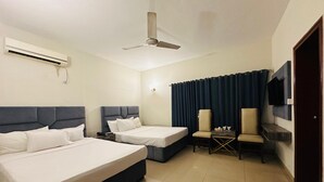 Een hotelkamer met twee bedden, een plafondventilator, een airconditioner, een aan de muur bevestigde televisie en een donker gordijn.