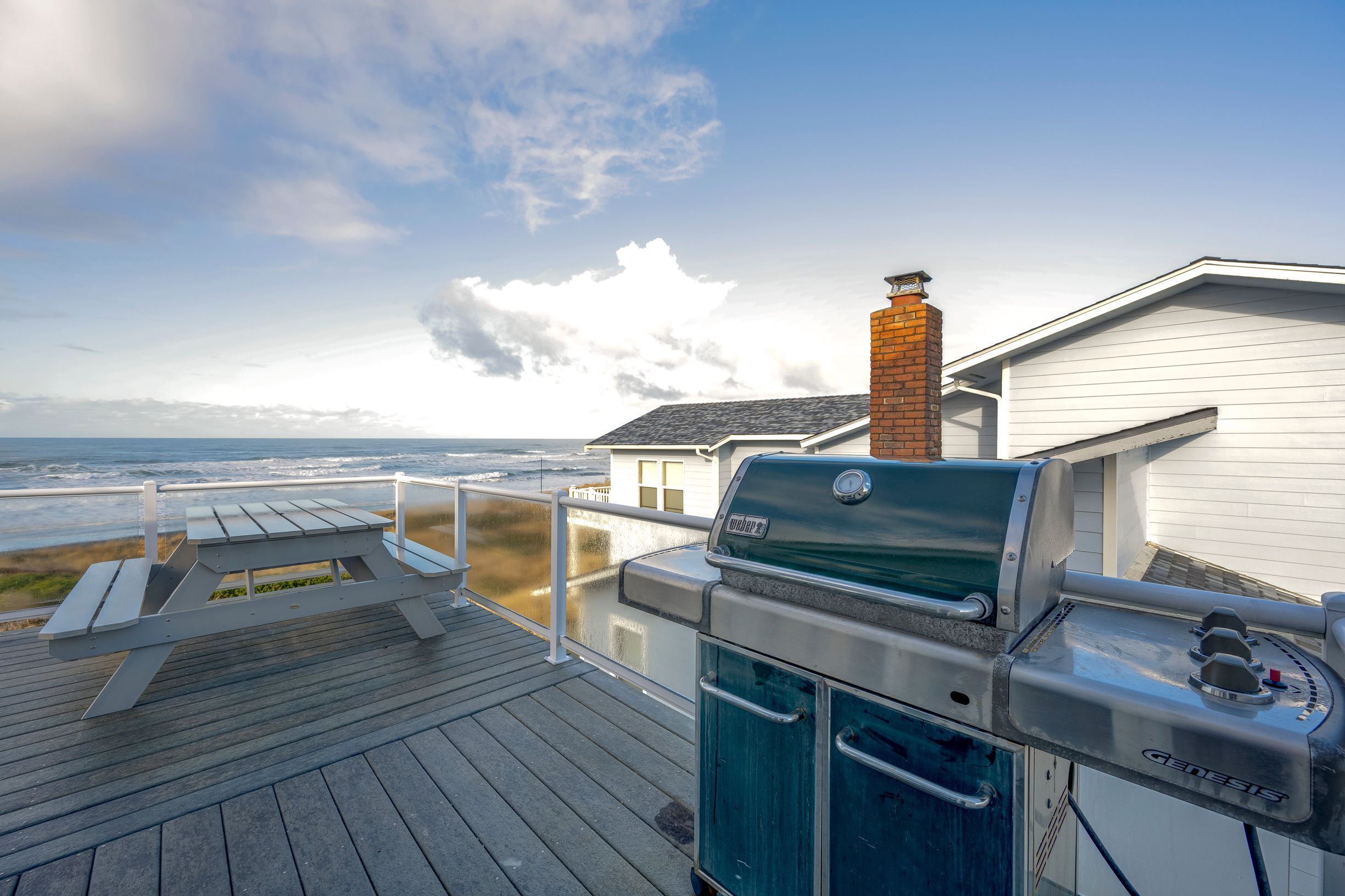 A deck with a grill and a view of the ocean.