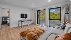A modern living room with a sofa, a dining table, and a TV. - Arawata Alpine Views - 2BDRM luxury (Queenstown)