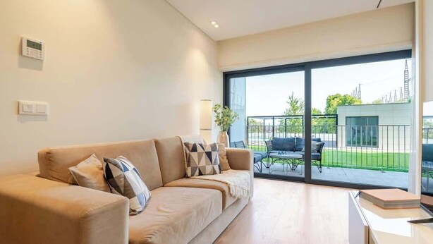 Een moderne woonkamer met een beige bank, een bijzettafeltje en een uitzicht op het landschap door grote schuifdeuren.
