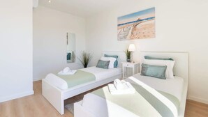 Une chambre moderne avec deux lits, un tableau représentant une plage et une table de chevet avec une lampe.