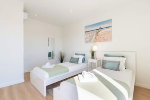A bedroom with two beds, a painting of a beach scene, a bedside table with a lamp, and a mirror on the wall. - Bright & Spacious Retreat with Balcony by HostWise (Porto)
