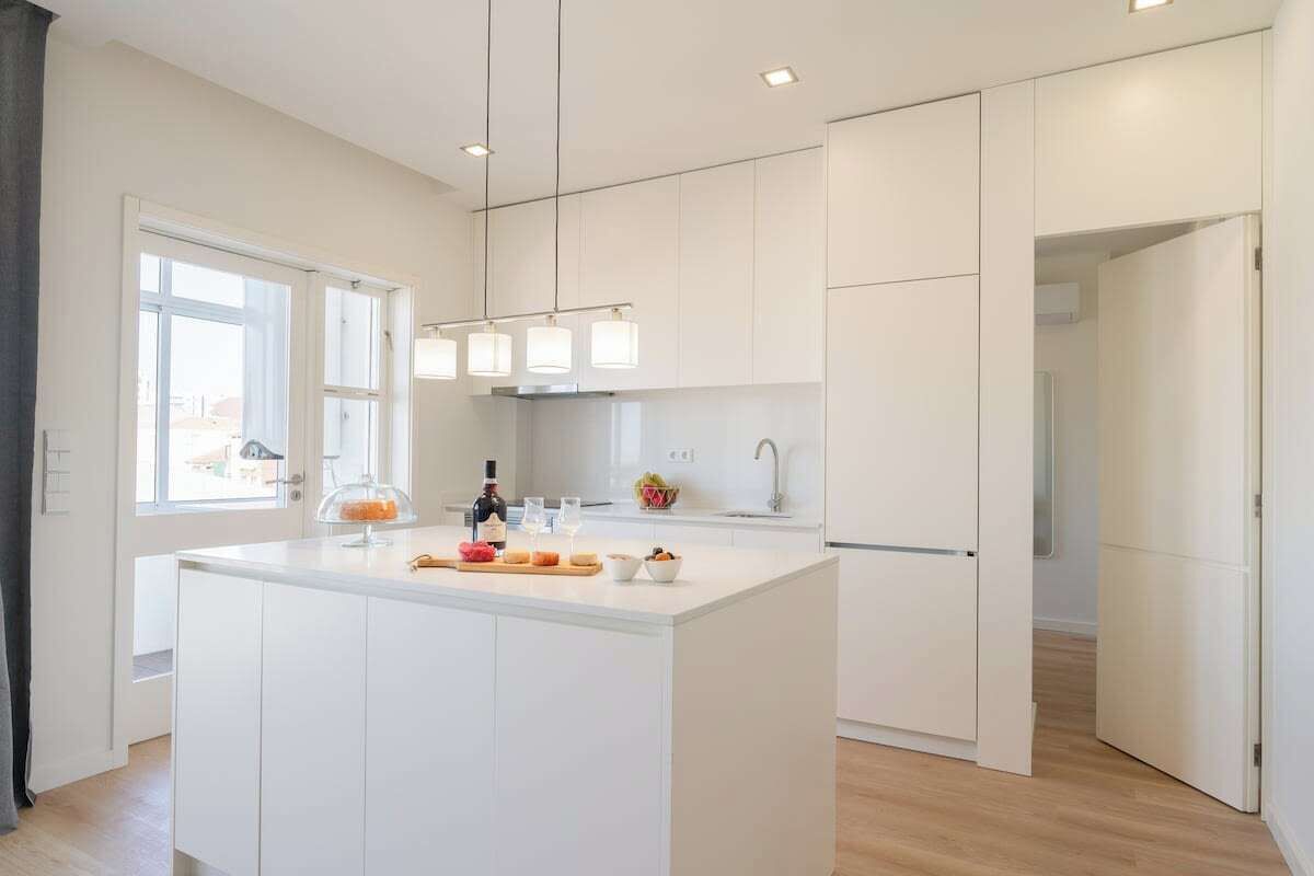 A modern kitchen with white cabinetry, a central island with a glass-top, and pendant lighting.