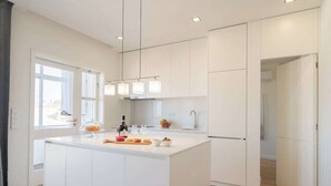 Une cuisine moderne avec des meubles blancs, un îlot central doté d’un plan de travail en verre et des luminaires suspendus.