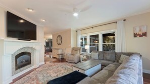 A living room with a fireplace, a large TV, a ceiling fan, and a sofa. - Lake Norman Retreat w/ Pool, Hot Tub & Private Dock Lake Life Cove by Avantstay (Mooresville)