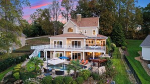Una casa de dos pisos con una terraza grande, una piscina y un jardín bien cuidado.