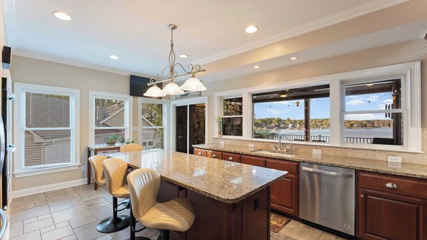 A modern kitchen with a large island, stainless steel appliances, and large windows offering views of a lake and trees. - Lake Norman Retreat w/ Pool, Hot Tub & Private Dock Lake Life Cove by Avantstay (Mooresville)